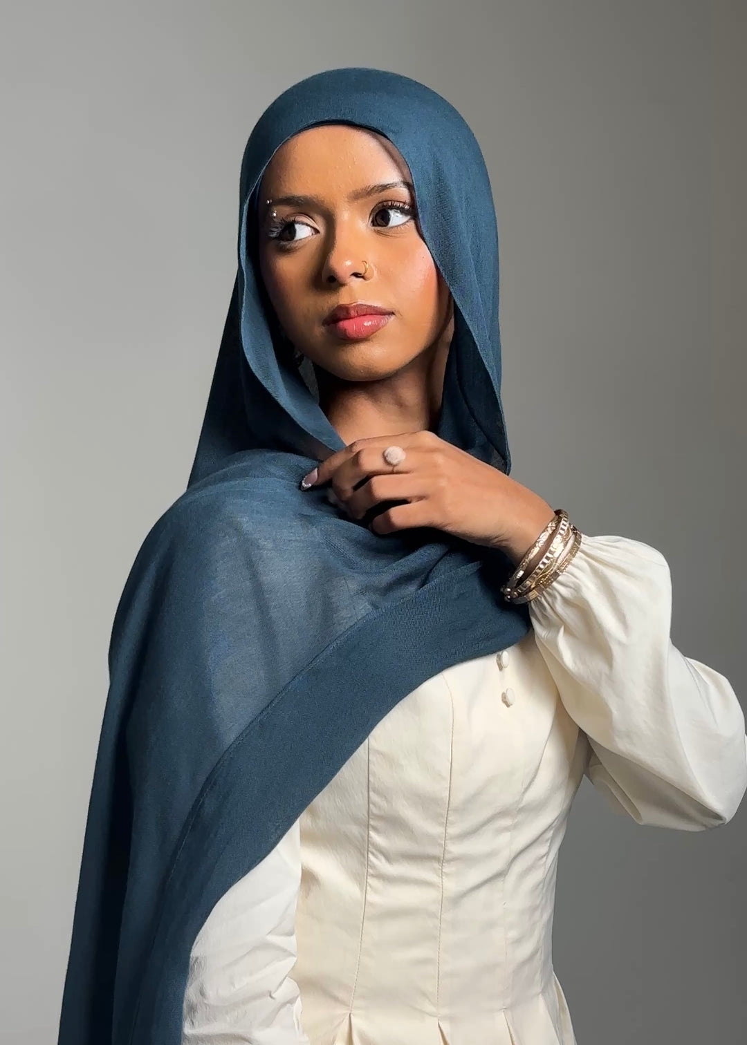 Woman wearing a blue hijab and white outfit against a gray background